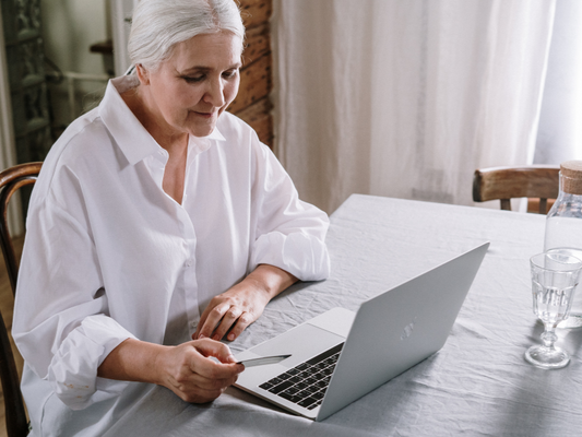 Ältere Frau am Tisch tippt mit einer Kreditkarte in der Hand auf ihrem Laptop, um online den Pflegegrad zu beantragen.