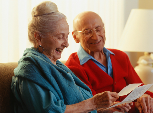 Ältes Ehepaar sitzt auf dem Sofa und liest glücklich einen Brief, symbolisiert die Vorteile der kostenfreien Pflegehilfsmittel durch die Pflegebox